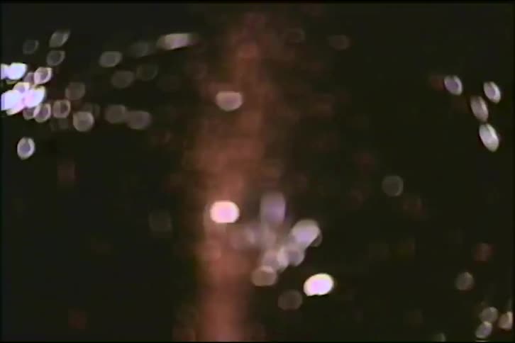 A vintage close-up shot of a single firework fountain erupting with sparks against the night sky, transitioning into a blurry bokeh effect