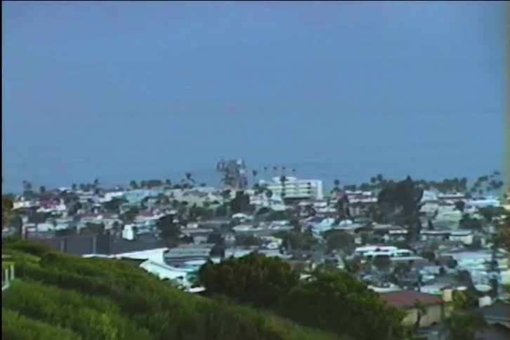 Vintage footage of a coastal town with a pier slowly zooms out to reveal the seaside landscape at dusk