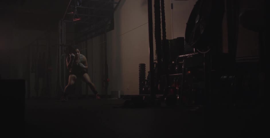 Woman practicing boxing under rope in dark gym