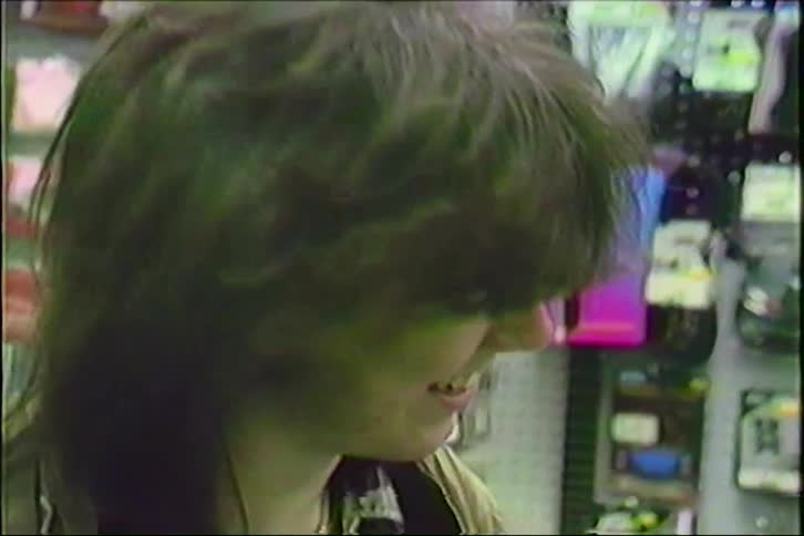 A young man with 80s hair smiles at the camera while shopping in a music store in this vintage VHS footage