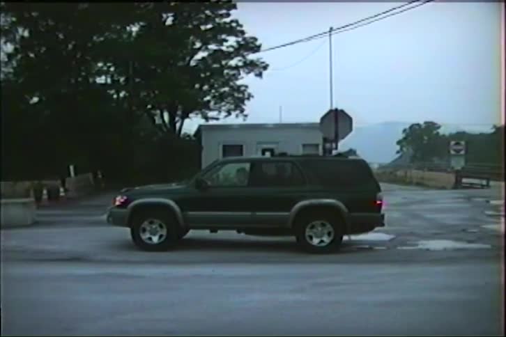 Vintage VHS footage shows a dark green SUV parked at a rural intersection on an overcast day