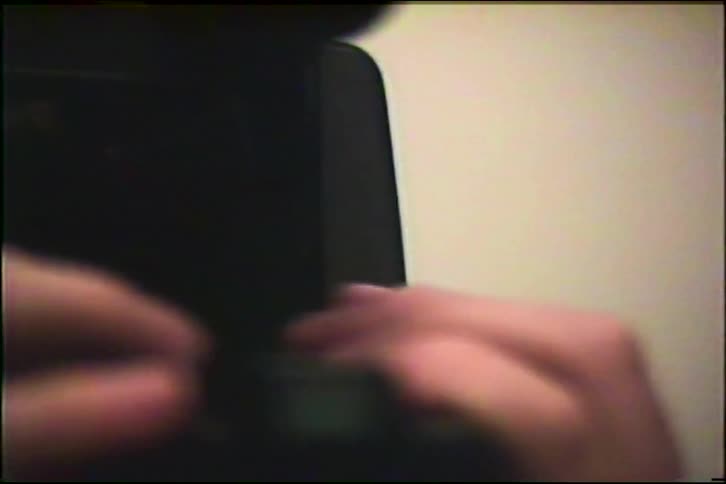 A young boy with ginger hair playfully films himself in a mirror with a vintage VHS camcorder