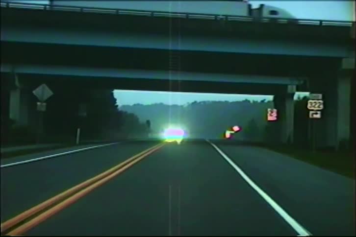 POV footage from a vintage home video shows a car driving on a wet highway at dusk toward an overpass as another car approaches