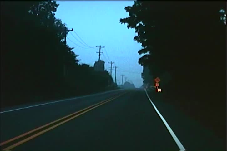 An eerie point-of-view drive down an empty rural highway through dense fog at dusk