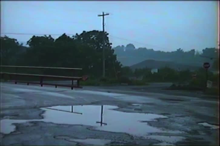 A slow zoom out from a puddle reflecting a utility pole on a gloomy, overcast day