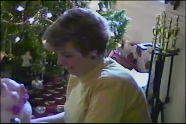 A woman smiles as she holds a cute piggy bank she received as a Christmas gift in front of a decorated tree