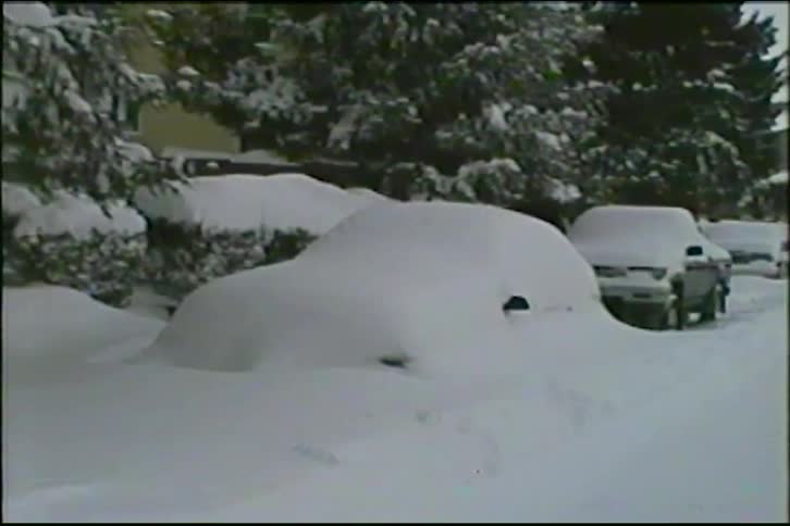 Vintage VHS footage pans across a row of cars completely buried under a thick blanket of snow