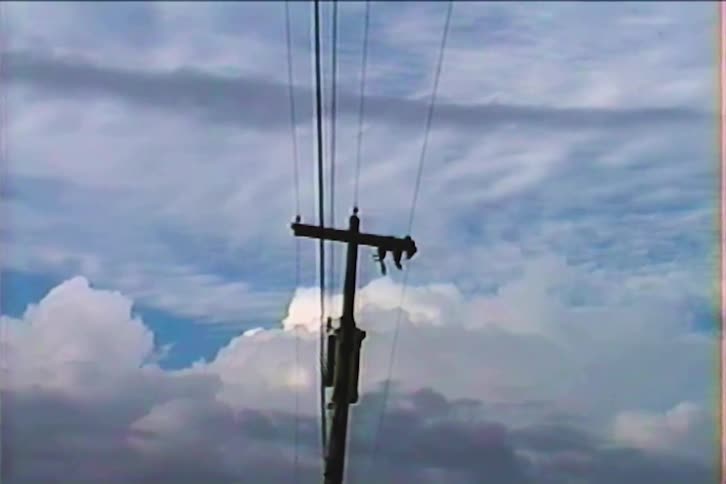 Retro home video footage shows a telephone pole silhouetted against a dramatic cloudy sky
