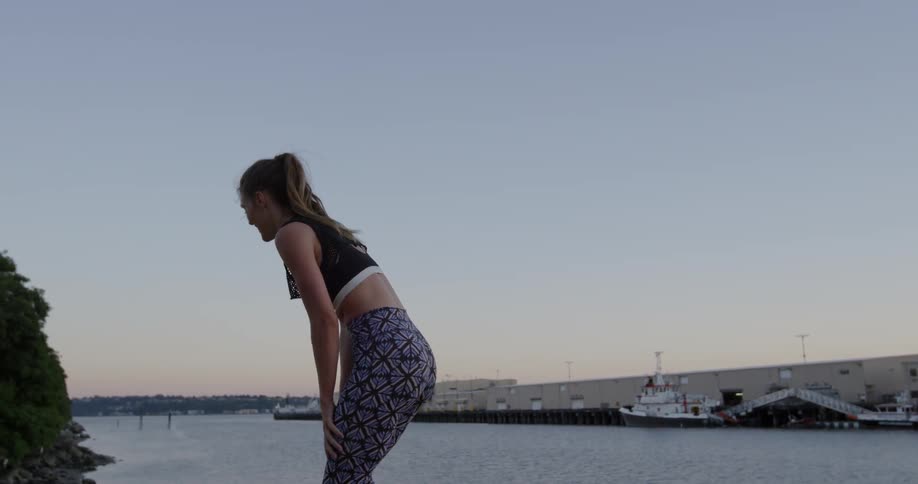 A woman in a sports bra leans over to catch her breath