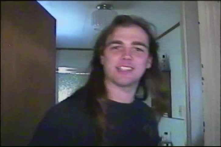 Vintage VHS footage captures a smiling young man with long hair before panning down to a young child playing with a stuffed animal