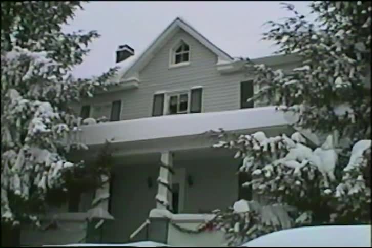 A slow pan up from cars buried in snow reveals a charming two-story house blanketed in a winter storm