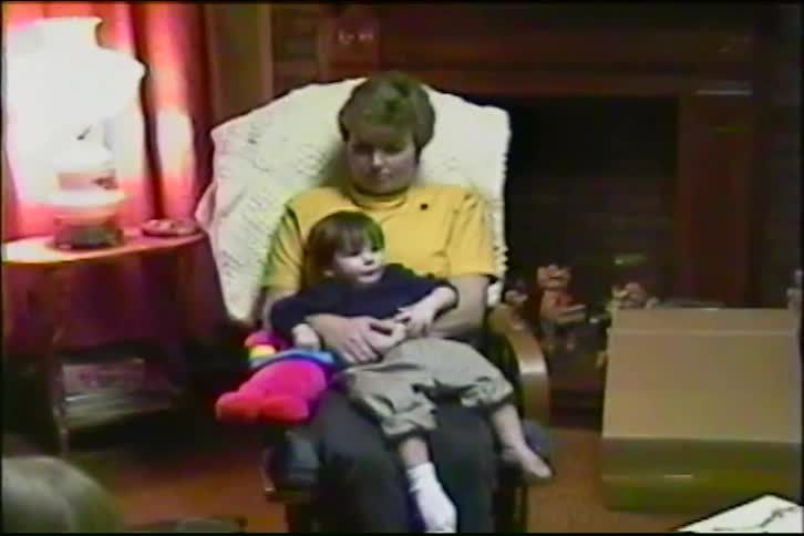 A loving mother gently rocks her sleepy toddler in a rocking chair in their cozy living room