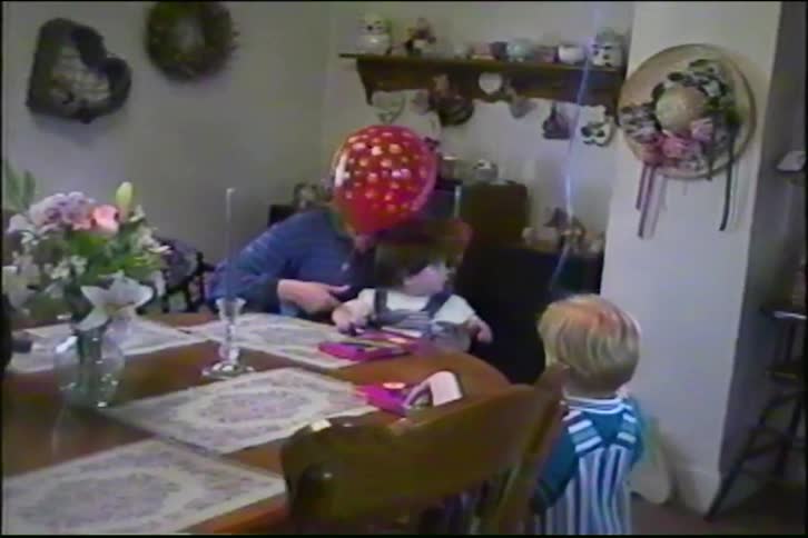 A mother and her children celebrate a birthday party at the dining room table with balloons in this charming home video