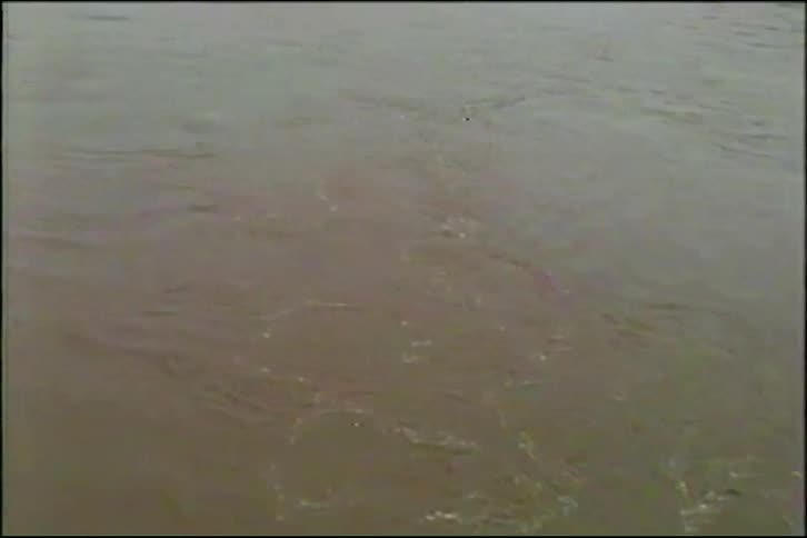 A close-up of churning, muddy water pulls back to reveal a wide, flooded river