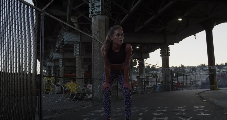 A woman leans over to catch her breath beneath a city bridge