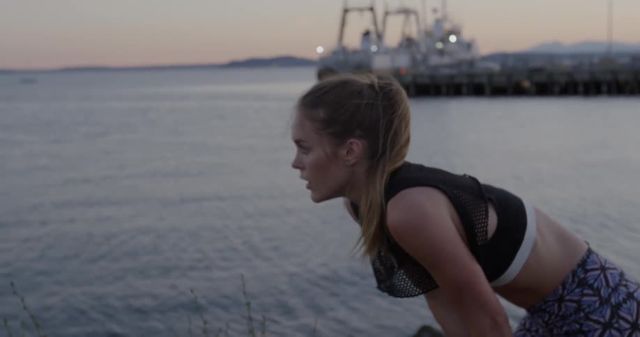 A woman walks by the water and bends down