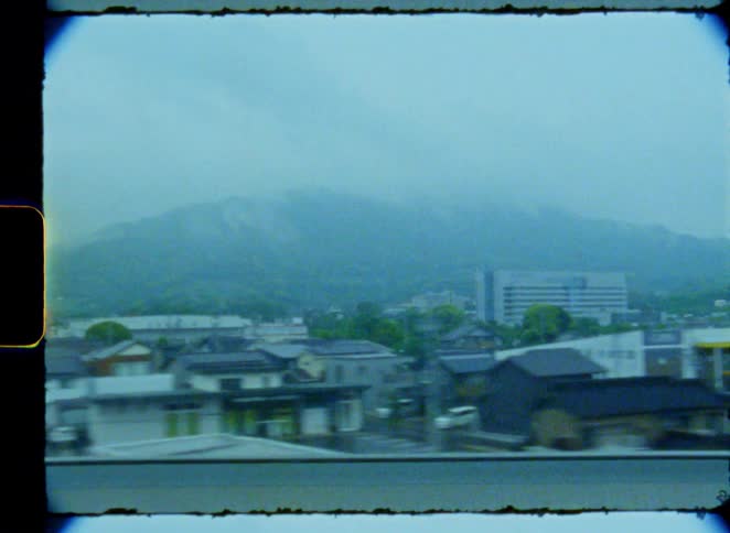 A dreamy, vintage-style view from a moving train captures a Japanese town nestled against foggy mountains