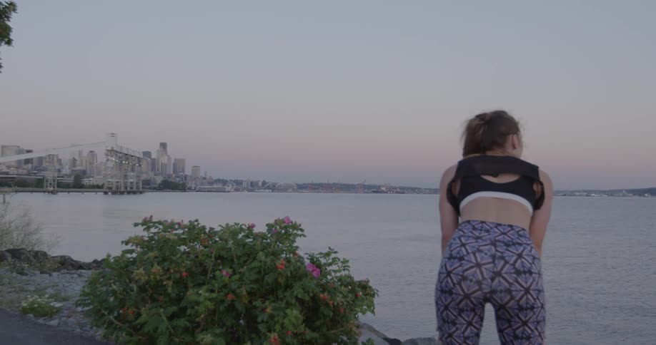 A woman leans over to catch her breath next to a lake at sunset
