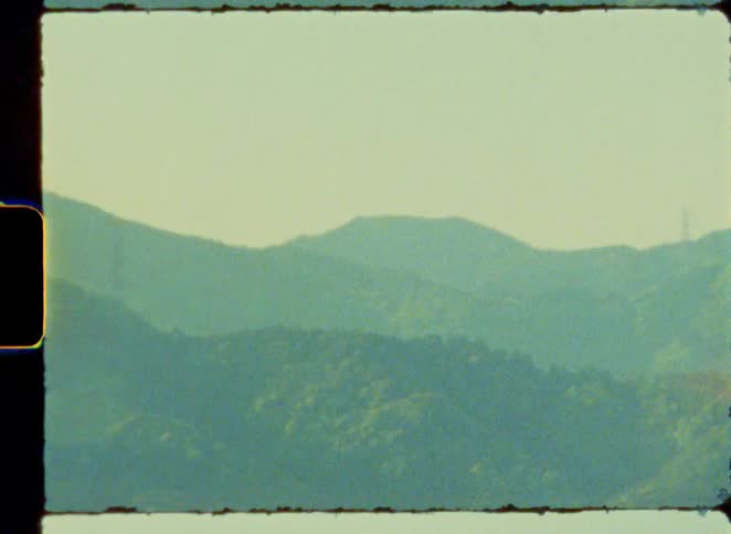 A vintage 8mm film captures the blurry, dream-like scenery of rolling green hills and countryside from a moving train window