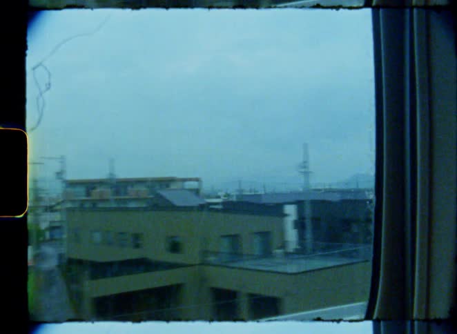 A vintage 8mm film captures the view of a Japanese town passing by from a train window on a gloomy day
