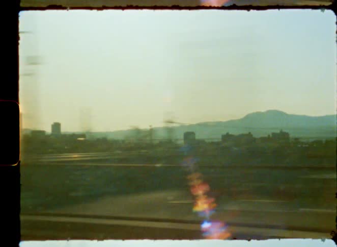 Abstract view from a moving train window showing a sun-flared city landscape on vintage 8mm film