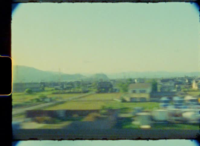 Vintage film captures the point-of-view from a moving train passing through the suburbs and into the rural countryside of Japan