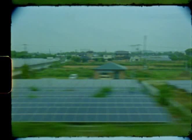 Vintage 8mm film captures the view of a Japanese river and solar farms from a moving train on an overcast day