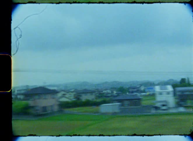 A nostalgic view from a train window shows the passing Japanese landscape of fields and houses on 8mm film