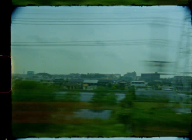 Vintage 8mm film captures a blurry view of the Japanese countryside and a solar panel farm from a moving train window on an overcast day