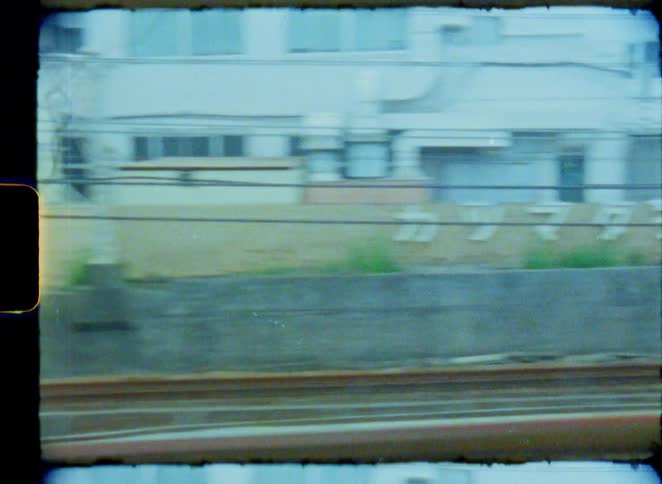 A nostalgic 8mm film point-of-view shot from a moving train captures the urban landscape of Japan