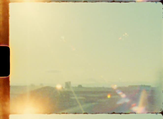 Authentic Super 8 film footage captures a blurry, sun-drenched landscape from a moving car window