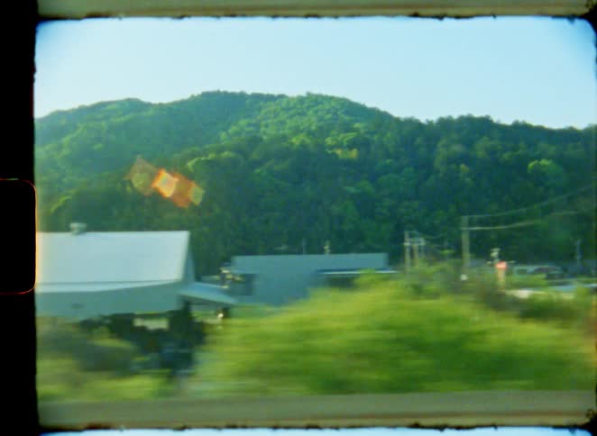An 8mm film captures the passing scenery of a Japanese rural town with green mountains in the background