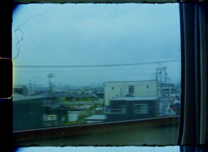 An authentic 8mm film captures the view of a Japanese city passing by from a train window on a gloomy day