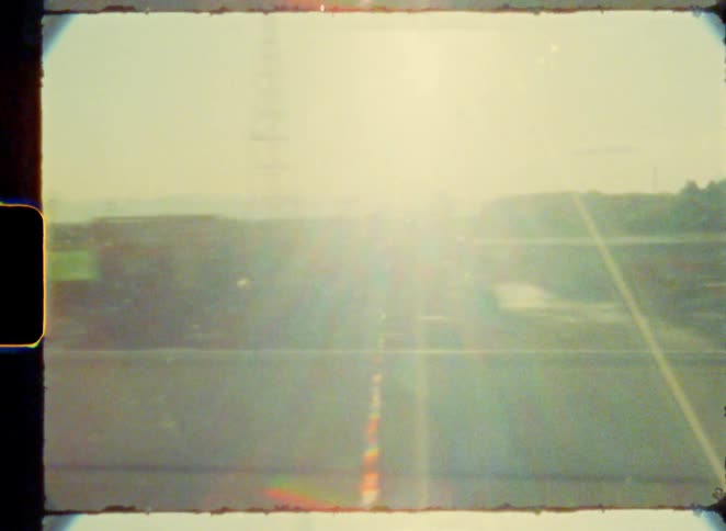 Blurry, sun-flared scenery passes by the window of a moving train in this authentic vintage 8mm film clip