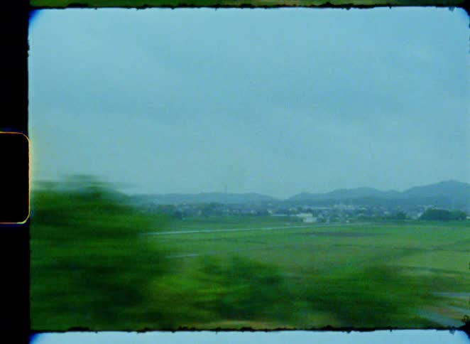A vintage film view from a moving train shows the lush green countryside of rural Japan passing by