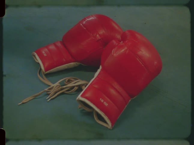 A hand grabs a pair of red boxing gloves from the canvas of a boxing ring in this vintage-style footage