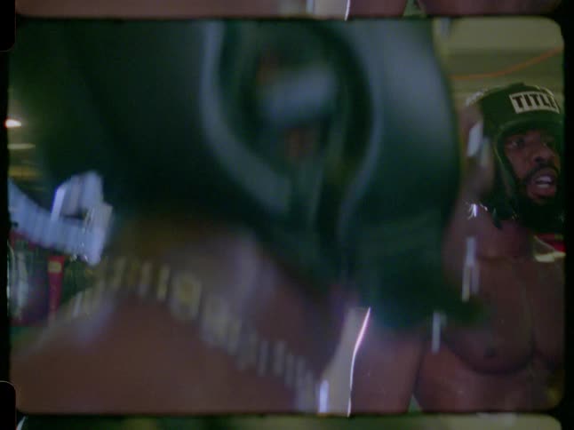 Vintage Super 8 footage captures a close-up profile of a sweaty boxer in headgear training in a boxing ring