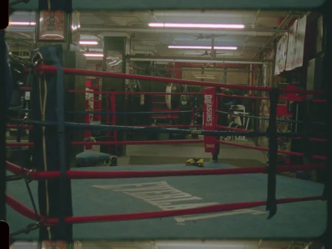 Vintage style film footage captures a still shot of an empty boxing ring in a gritty, classic gym