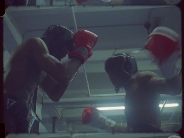 A low-angle, vintage film shot captures two boxers sparring intensely in a dimly lit, gritty gym