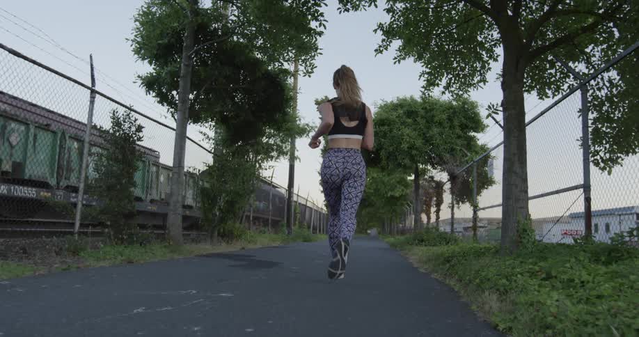 A woman is jogging on a fenced in path near train cars