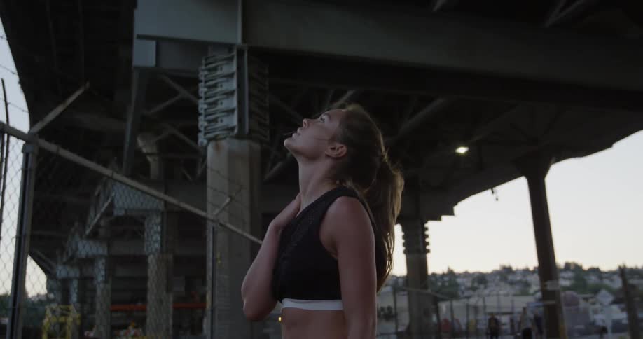 A female jogger is stopped under a bridge catching her breath