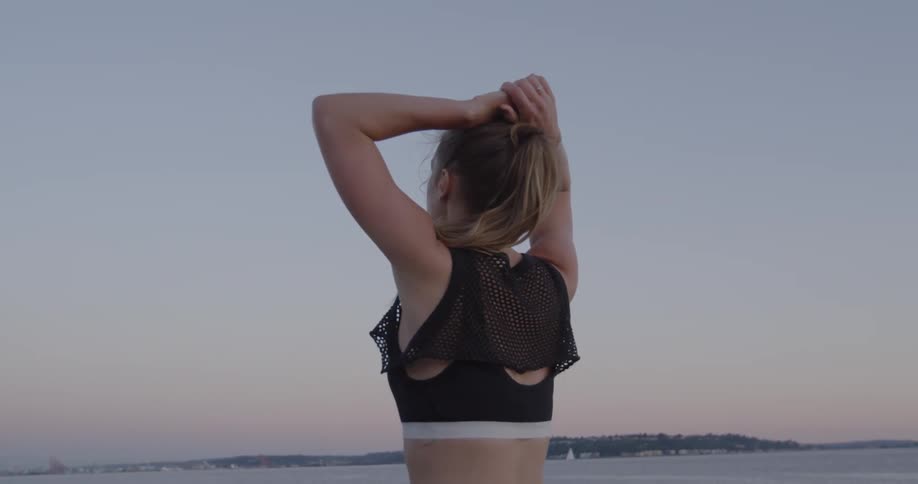 Woman looking at a large body of water while standing and resting her hands on top of her head