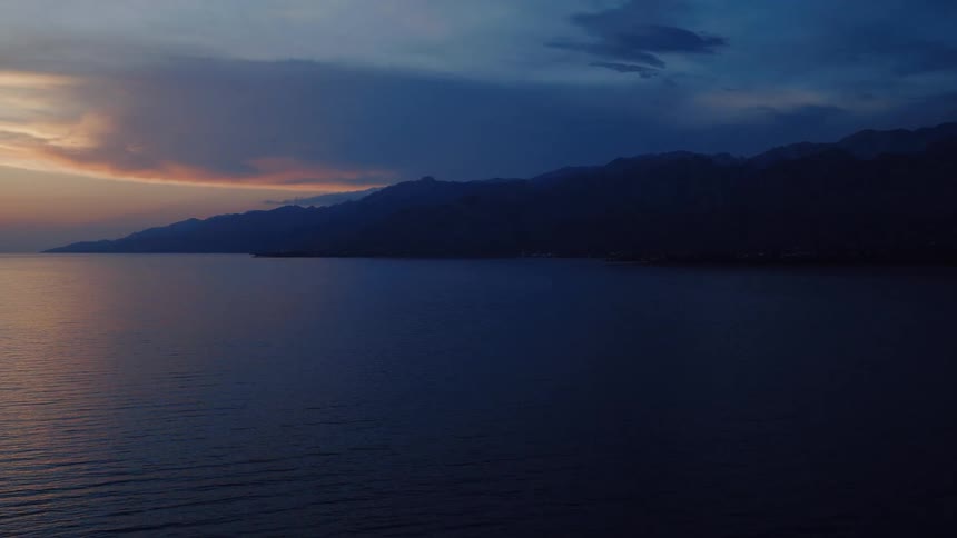 A dramatic timelapse reveals a vibrant sunrise over a tranquil sea, silhouetting a distant mountain range