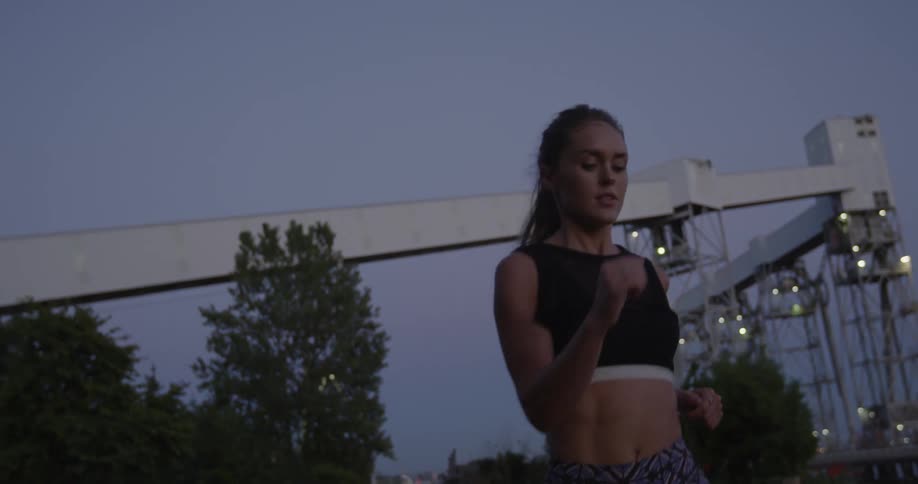 A woman jogs in a city park at dusk
