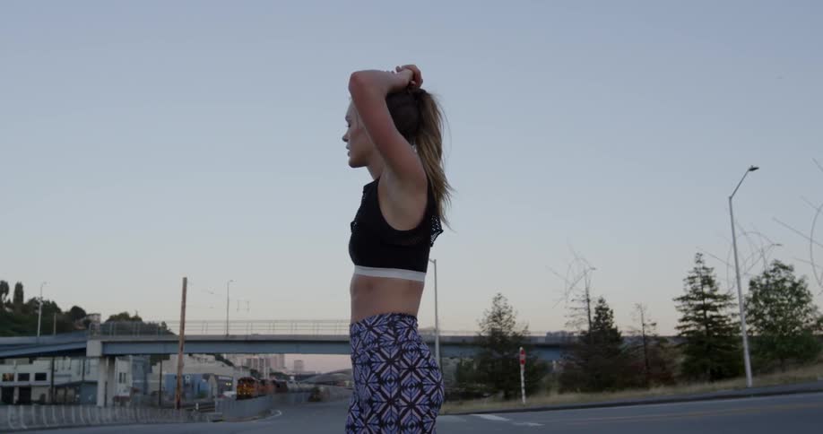 Woman stands with arms over her head looking down a city road