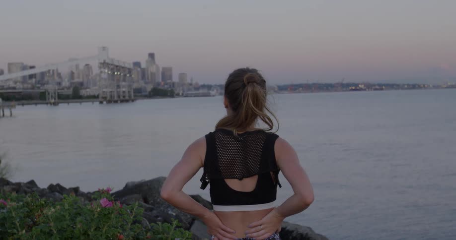 A female jogger is stopped at the edge of a harbor looking around