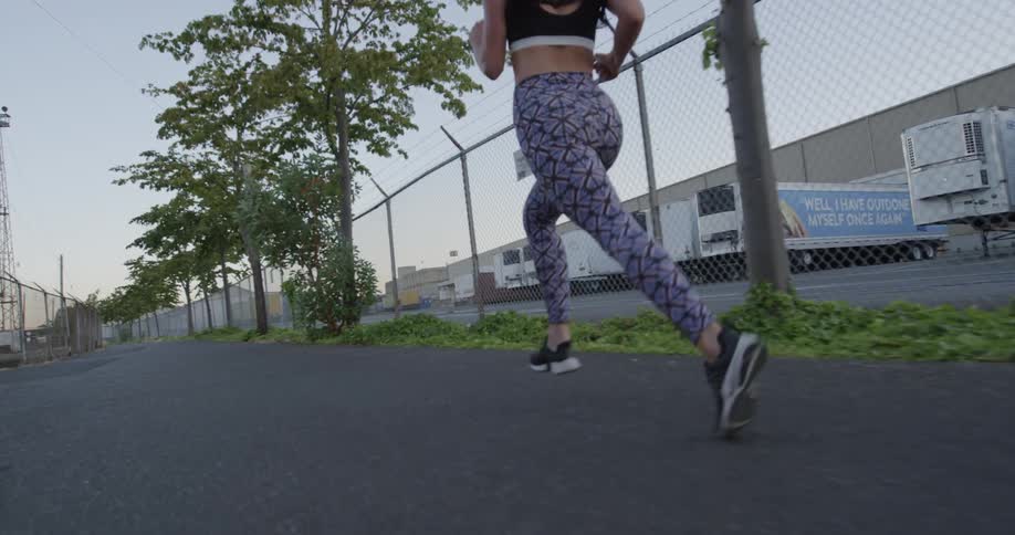 A woman jogs on a sidewalk near a warehouse