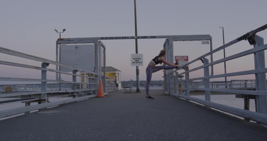 Woman stretching on a pier while putting her leg on the railing