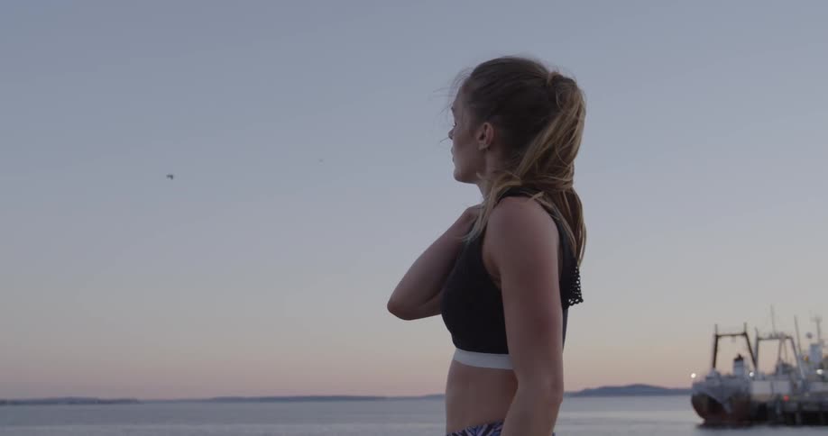 A female jogger is stopped at the edge of a harbor looking around