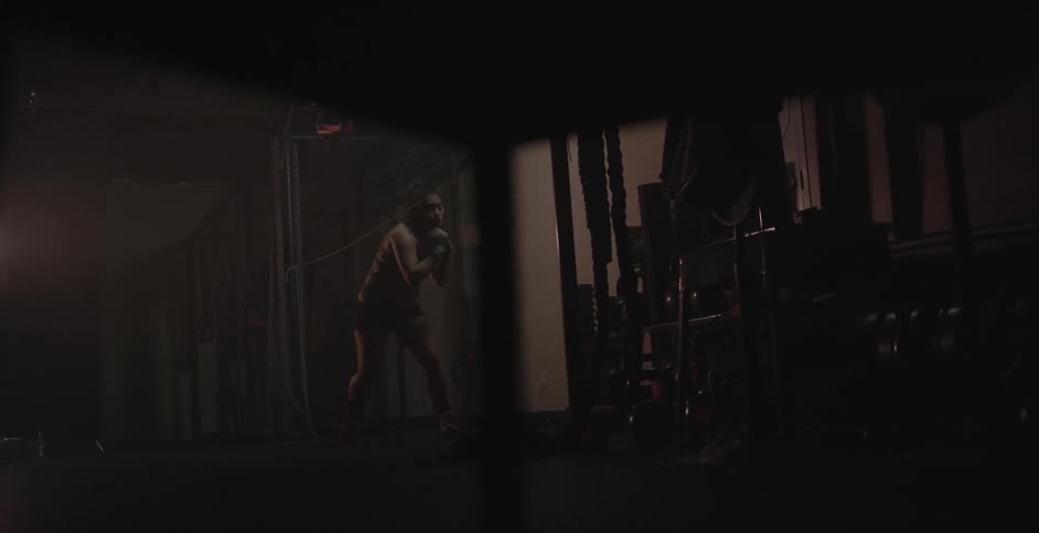 A woman spars and punches the air in a dark weight room